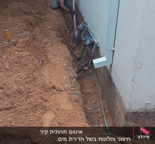 שני אנשים חופרים תעלה ליד קיר עם צינורות חשופים